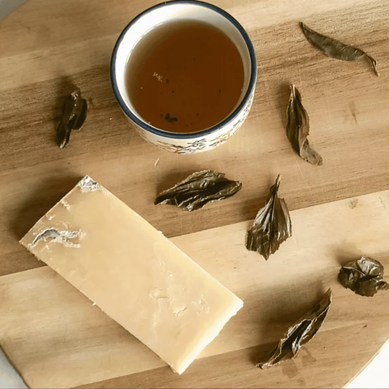 Découverte du thé en Île-de-France par une tasse de thé oolong fortement oxydée qui est posée sur une planche en bois en haut de la photo. En bas à gauche sur le même support, un fromage Cheddar est déposé. Plusieurs feuilles de thé infusées sont également disposées sur cette planche.