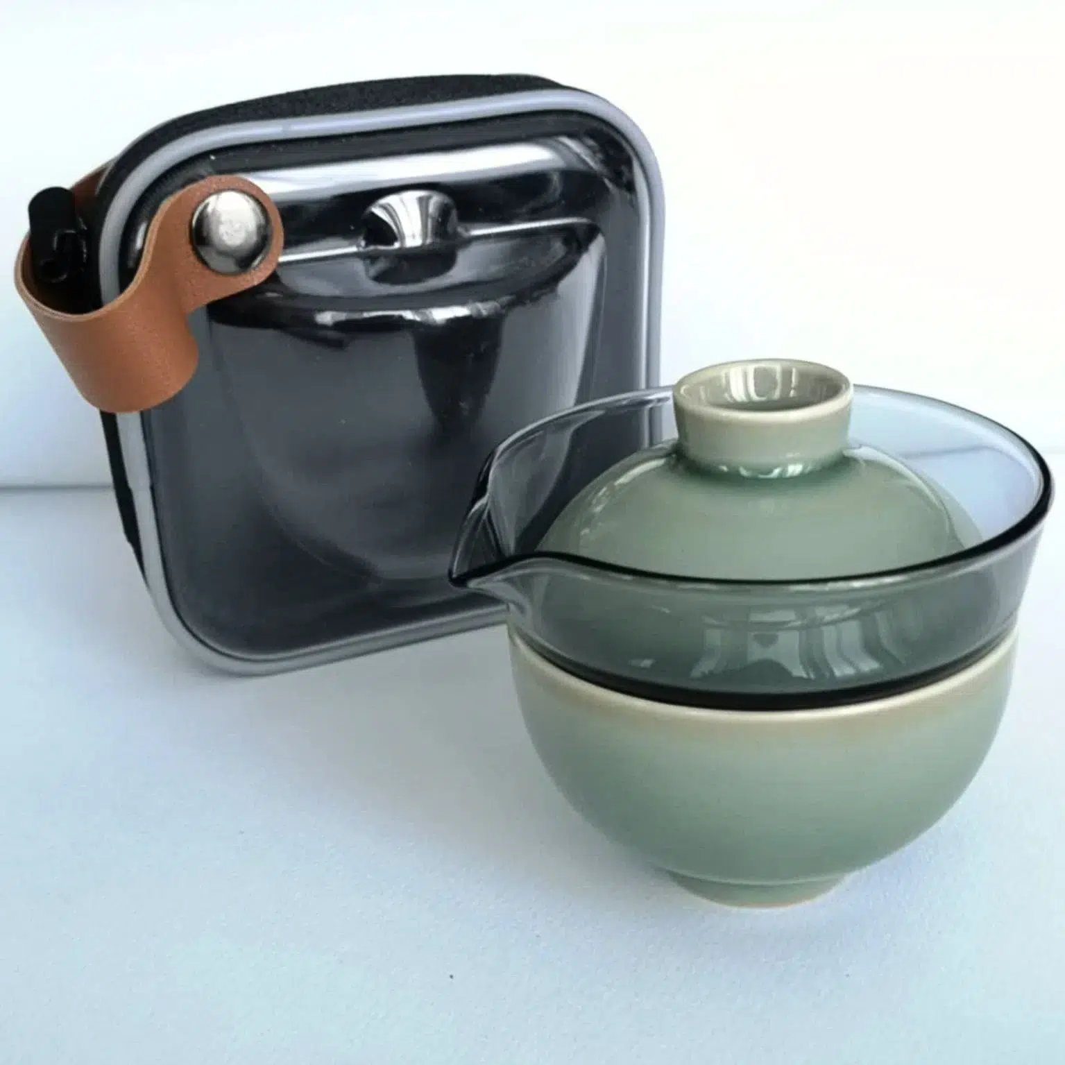 Photographie packshot d'un set de voyage comprenant une infuseur en verre avec son couvercle et la tasse en porcelaine couleur céladon avec une housse de transport.