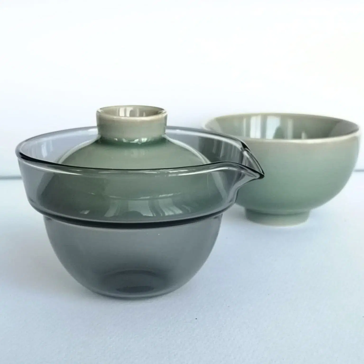 Photographie packshot d'un set de voyage comprenant une infuseur en verre avec son couvercle et la tasse en porcelaine couleur céladon.