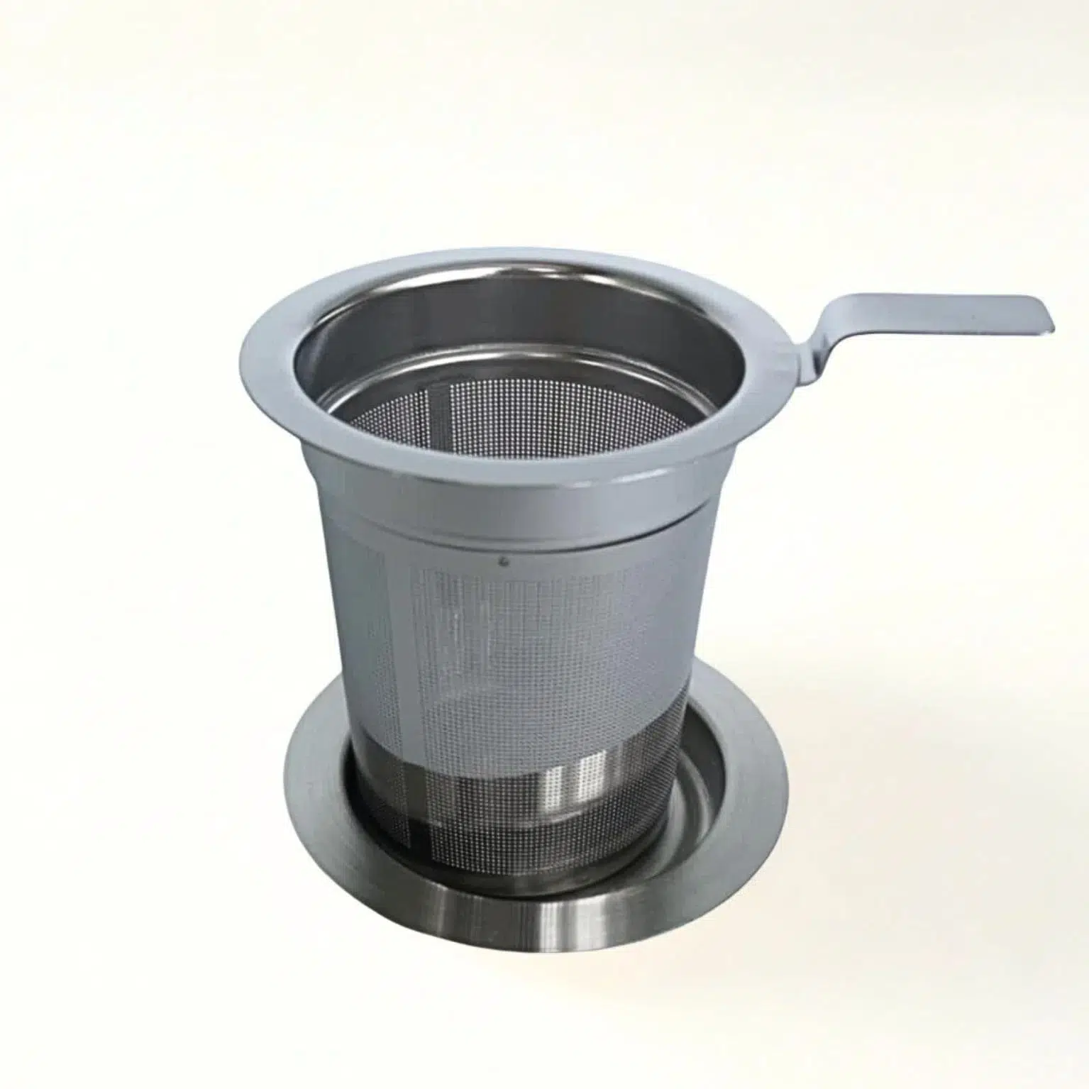 Photographie en packshot (fond neutre blanc cassé) d'un filtre acier inoxidable avec son couvercle qui sert aussi de coupelle