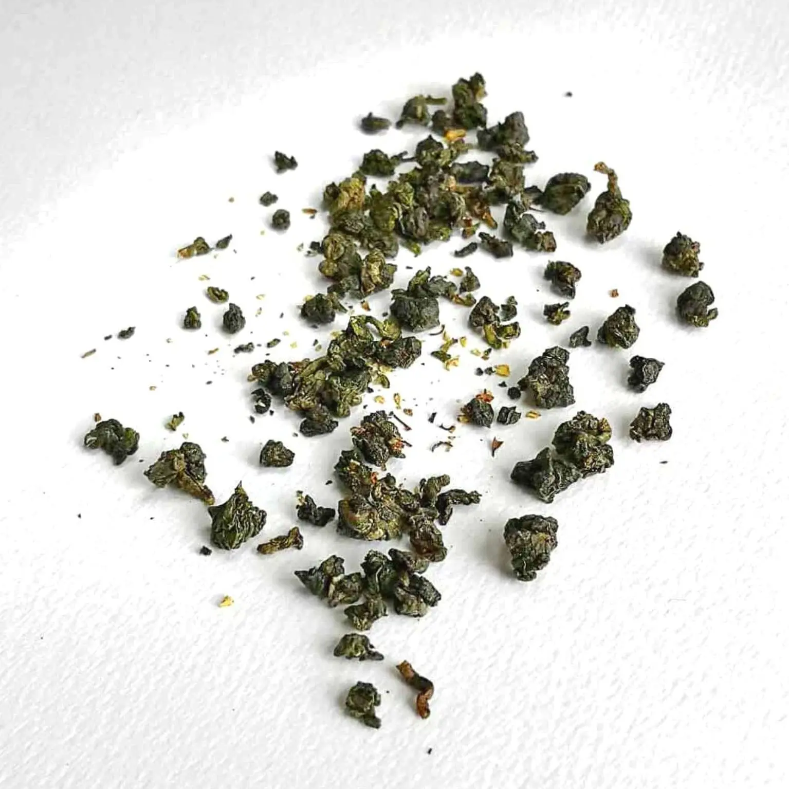 Photographie packshot sur fond blanc des feuilles du thé oolong Secret Osmanthus roulées en perles avec des fleurs jaunes d'osmanthes