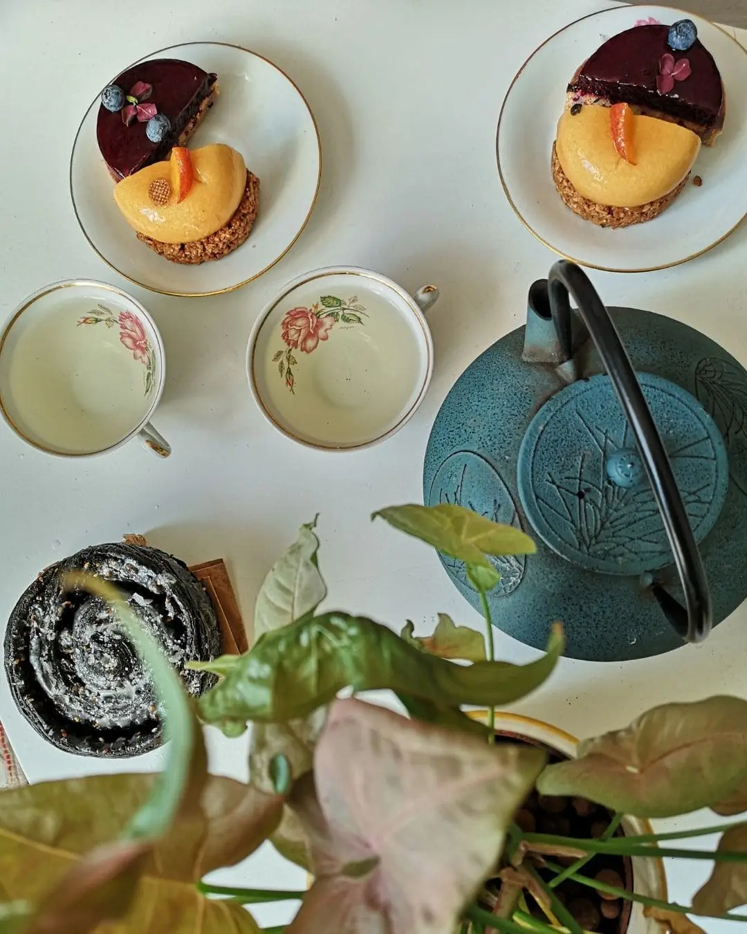 Photographie pour atelier "Accords Thés et Patisseries", on voit plusieurs patisseries sur des assiettes en porcelaine accompagnés d'une théière en fonte et des tasses à thé en porcelaine
