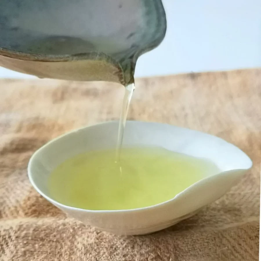 photographie pour l'atelier : "Le thé et Umami : compréhension et dégustation de la cinquième saveur" représentant une verse d'un thé vert dans une tasse à thé blanche en porcelaine posée sur un tissus beige.